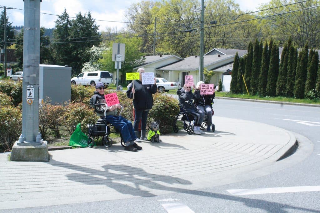 Older adults holding out protest signs by the side of the road.