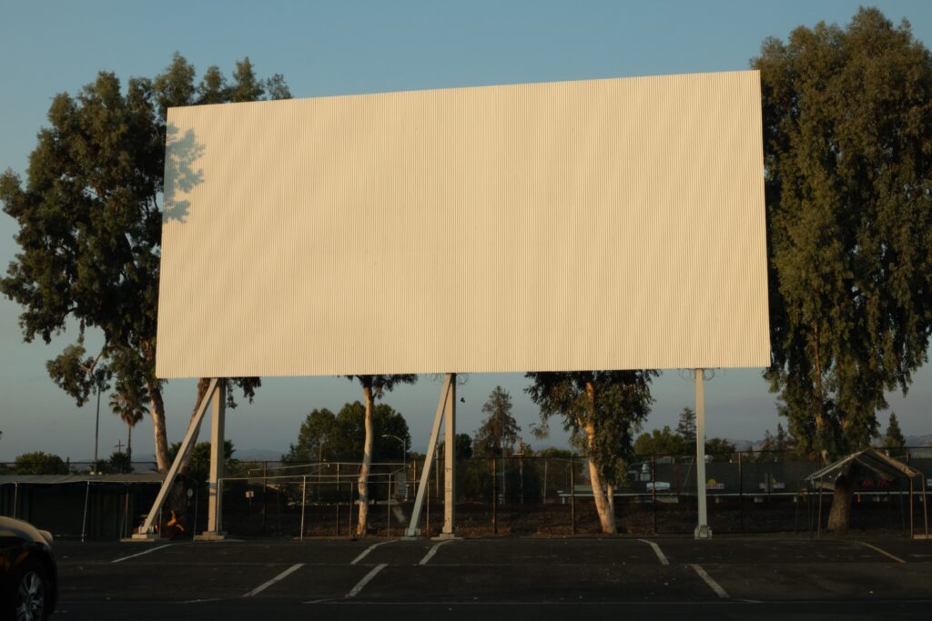 Blank billboard in a parking lot with trees in the background.