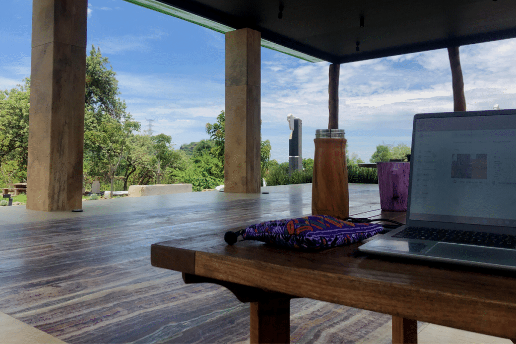 Laptop and coffee mug on a wooden table, trees and the sky in the background.