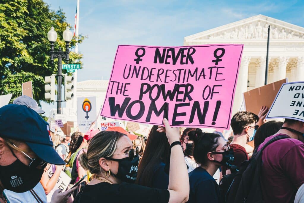 A person holding a pink sign that reads "Never underestimate the power of women!"