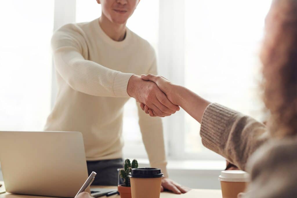 Man and woman shaking hands over a table. Newsletter swap. 